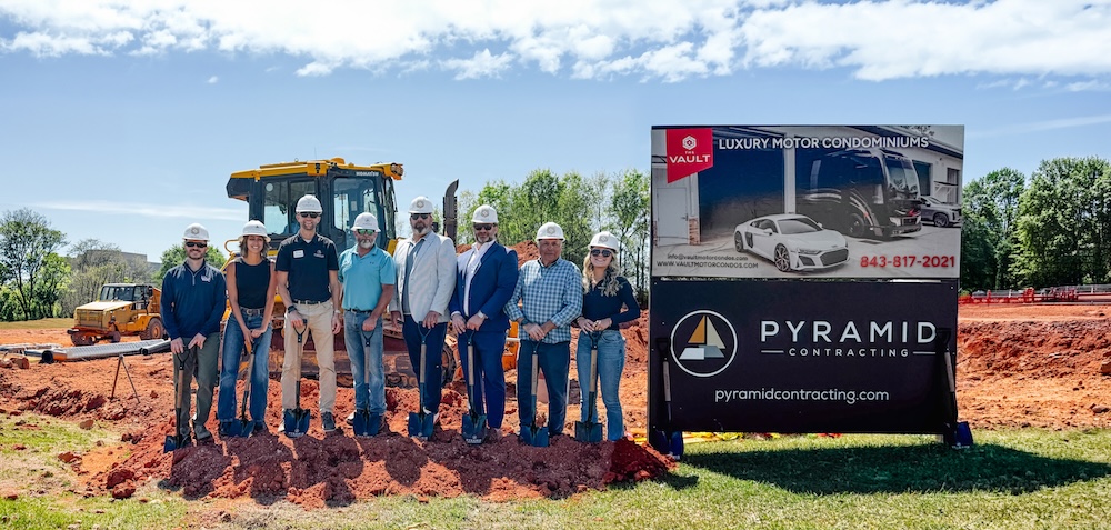 Group of construction workers and executives posing with shovels at a ground-breaking ceremony beside a Pyramid Contracting sign.