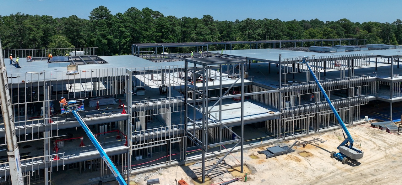 Pyramid Process - Pyramid Contracting Under-construction office building with exposed steel framework, scaffolding, and workers on different floors with blue boom lifts nearby.
